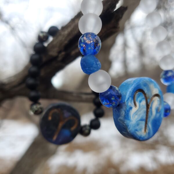 Two bracelets with Aries Zodiac sign charms, hanging from a tree branch.